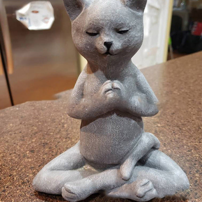Gray cat-shaped figurine sitting in a meditative pose on a brown surface.