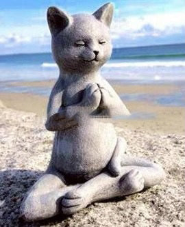 Stone cat sculpture meditating on a beach with ocean and sky in the background