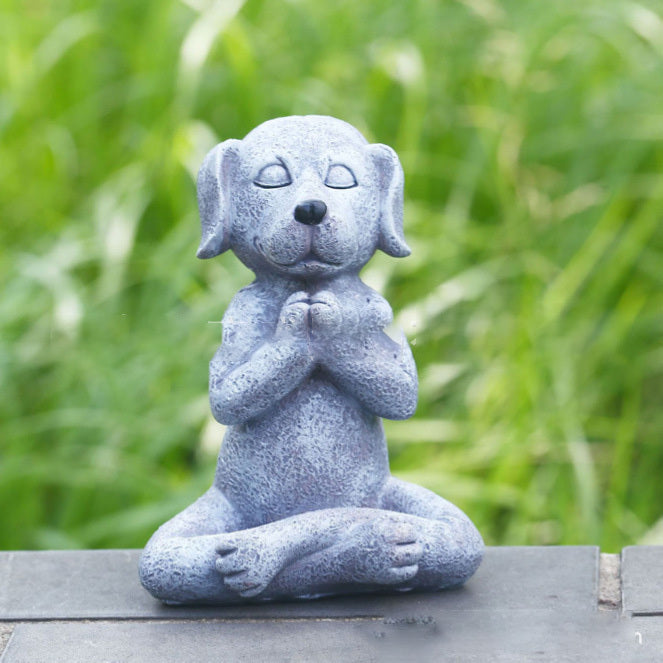 Stone dog sculpture in a meditative pose on a wooden surface with a grassy background